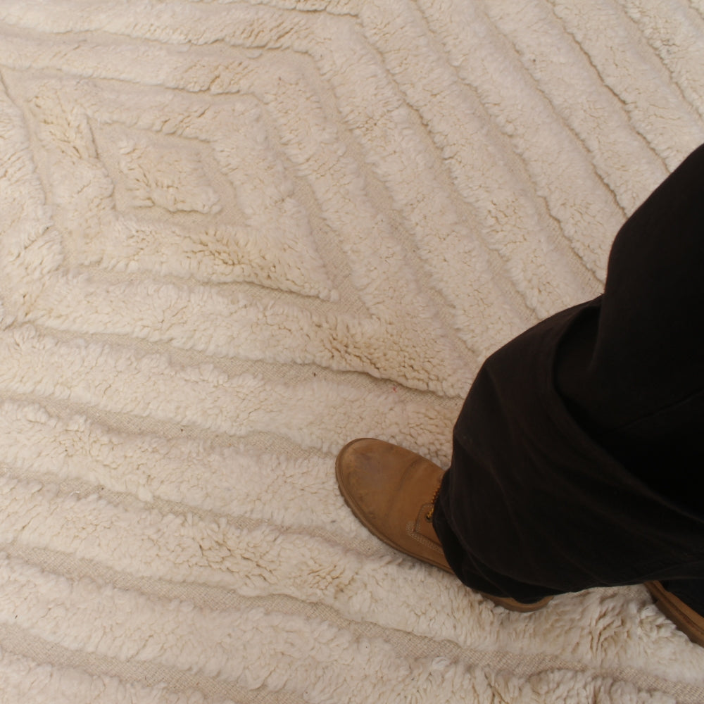 Close-up of a moroccan beni ourain carpet with a person's leg wearing brown shoes.