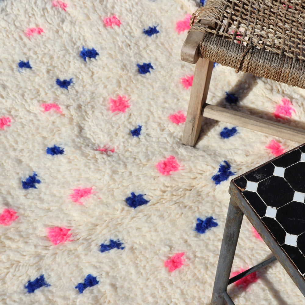 Close up of handwoven Beni Ourain wool rug, soft ivory pile with pink and blue berber motifs Moroccan artisan craftsmanship