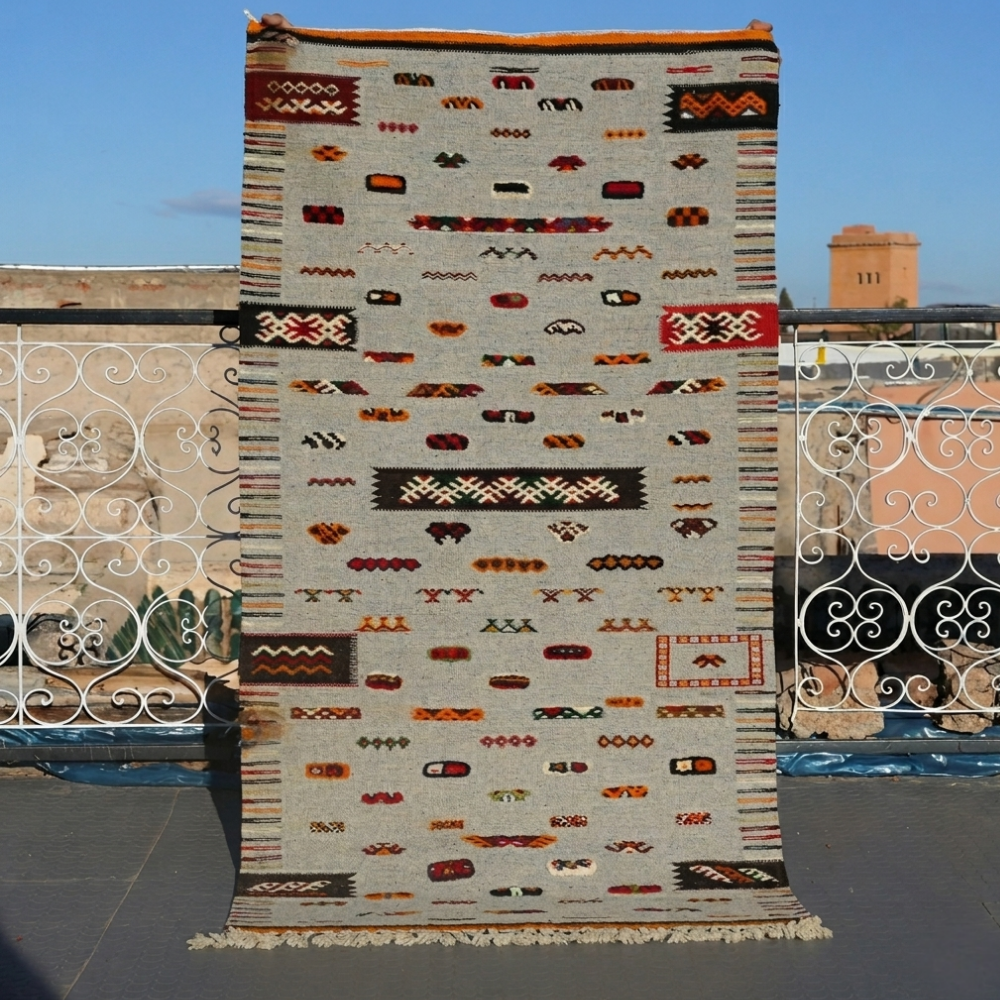 Handwoven Akhnif Moroccan rug with tribal Berber motifs in neutral wool tones displayed outdoors in Marrakech