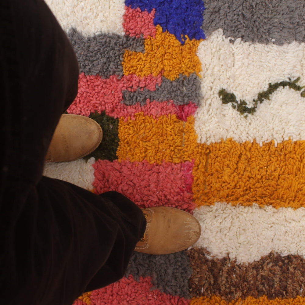 Person wearing brown boots stepping onto a colorful boujaad rug.