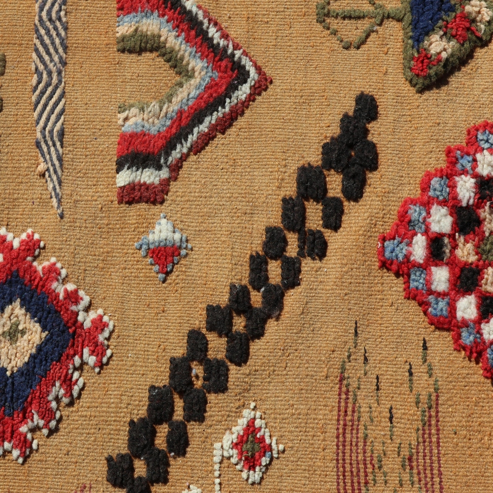 Close up of a textured geometric tribal patterns in red, blue, and black on a brown rug.