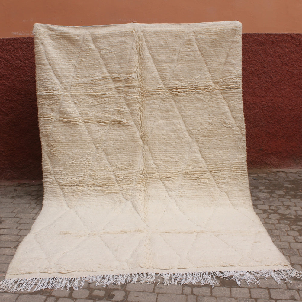 Textured beige rug with frayed edges on a red brick wall background