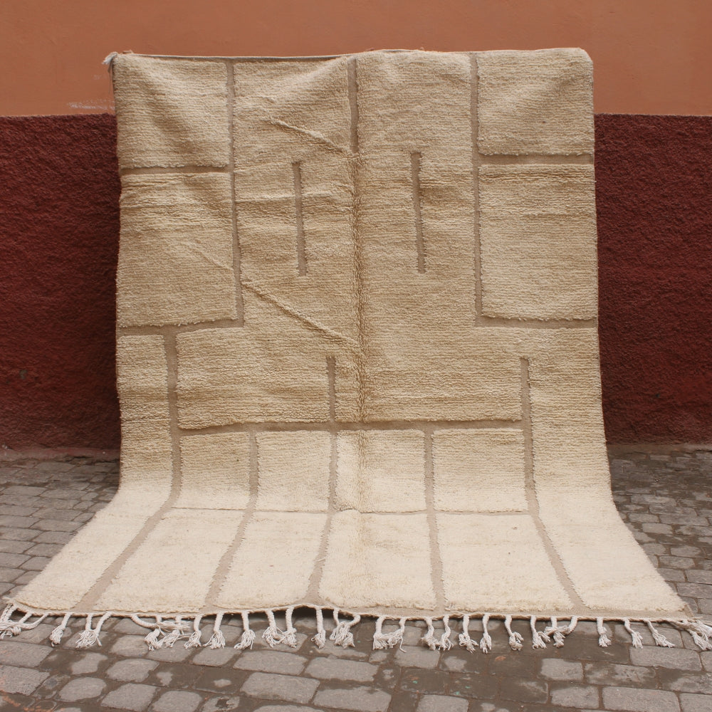 Beige woven rug with geometric pattern on a red brick wall background