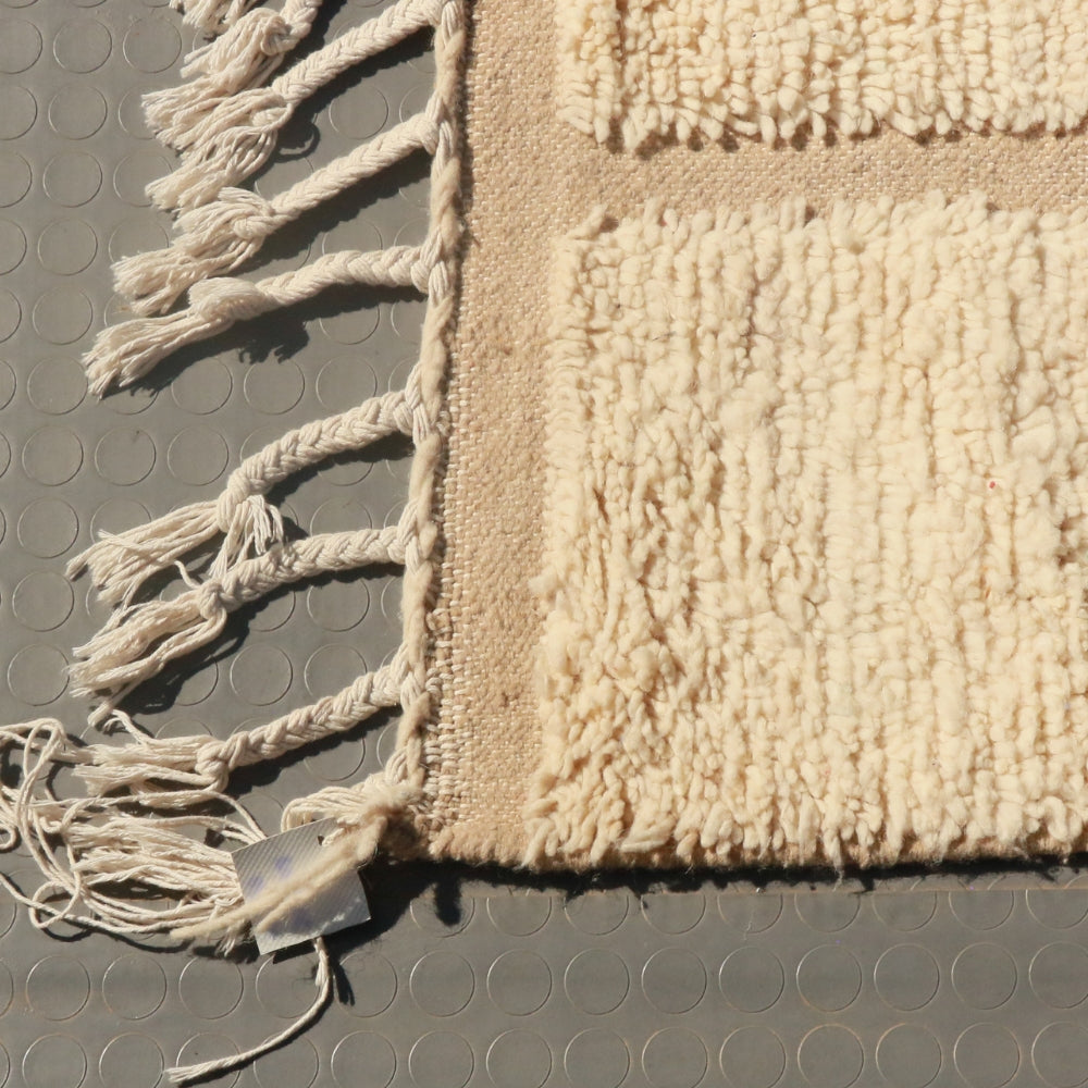 Beige textured rug with tassels on a gray surface