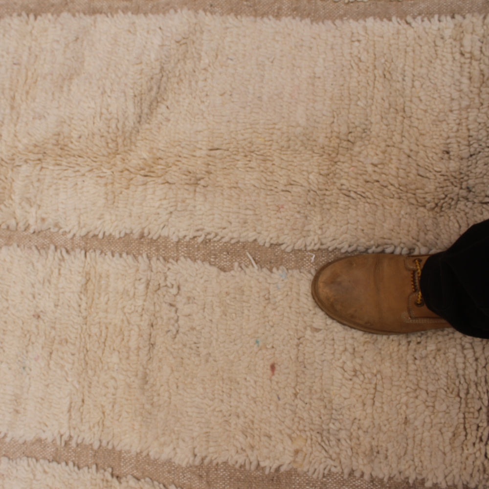 Brown shoe stepping onto a beige beni ourain carpet